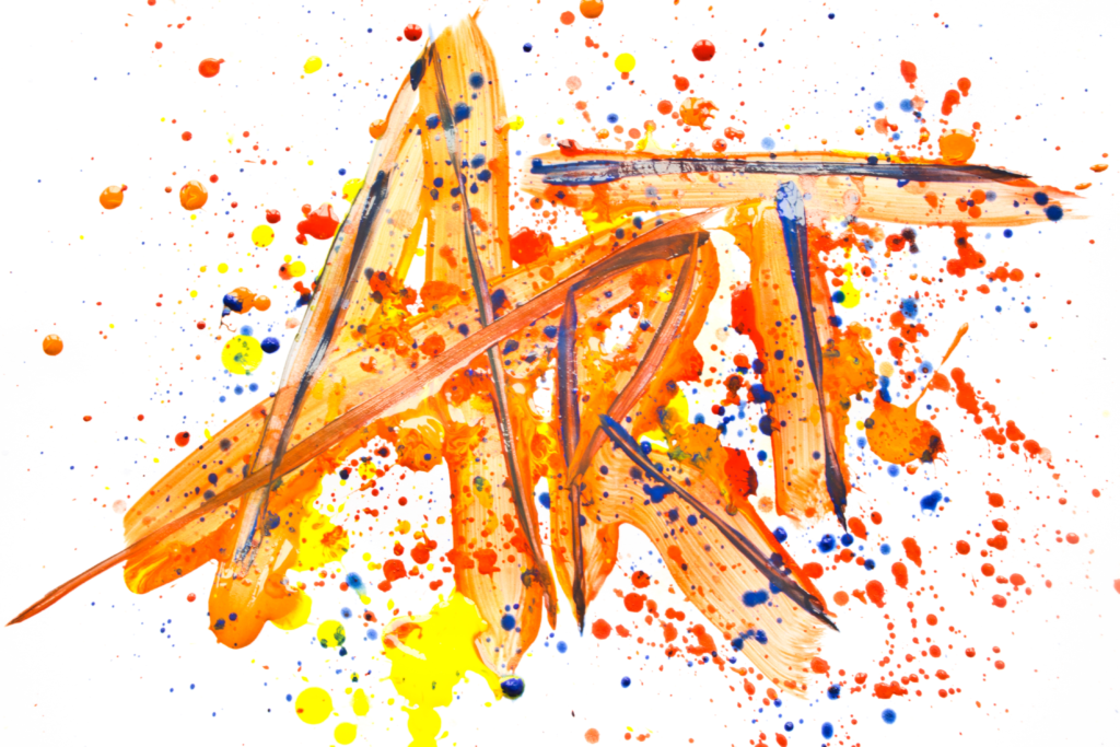 The word ART painted in orange acrylic paint and splatter of many other colors.
