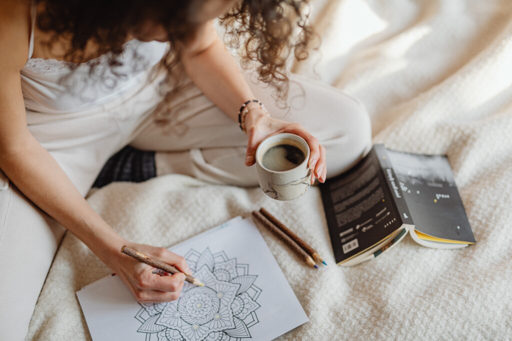 adult woman sittingon bed with coffee coloring a mandala