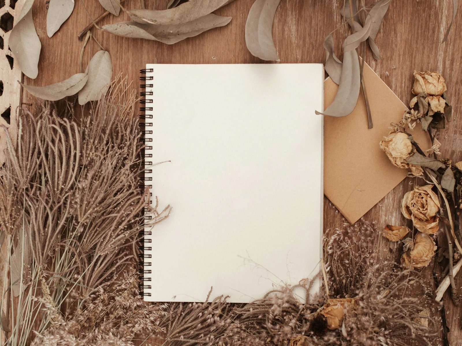 A blank notebook surrounded by dried flowers offers a rustic, creative background.