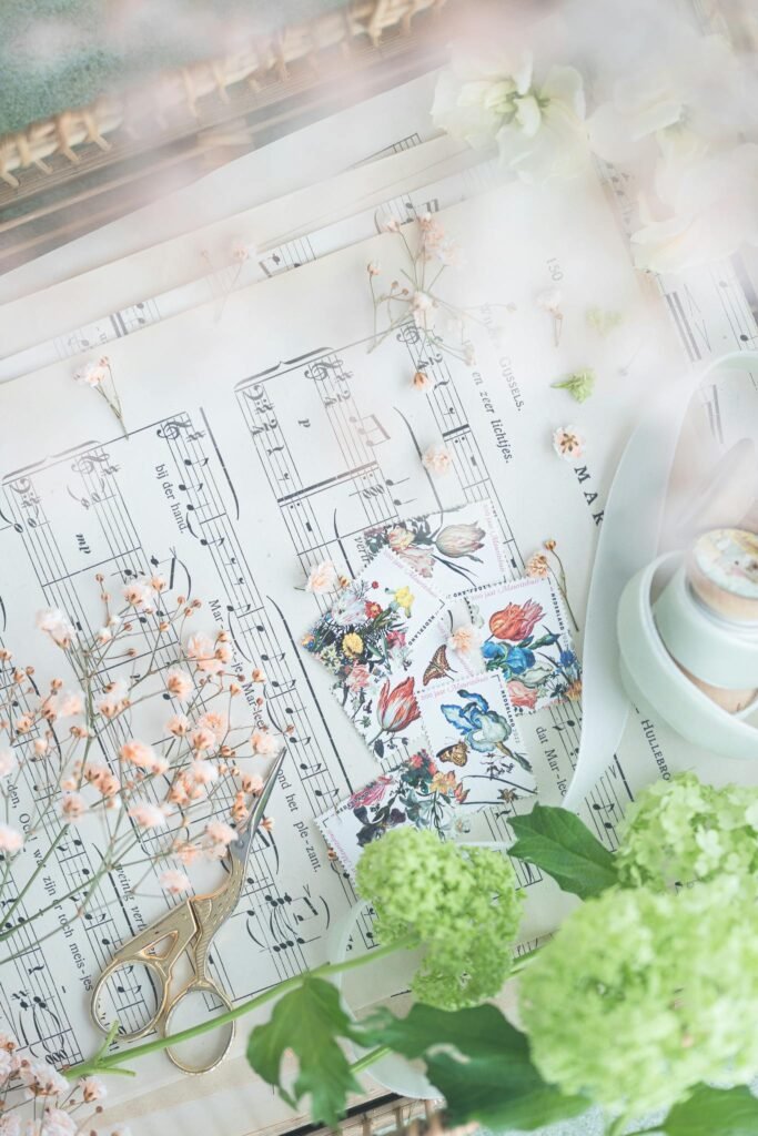 Delicate flatlay with flowers, music sheets, scissors, and decorative stamps.
