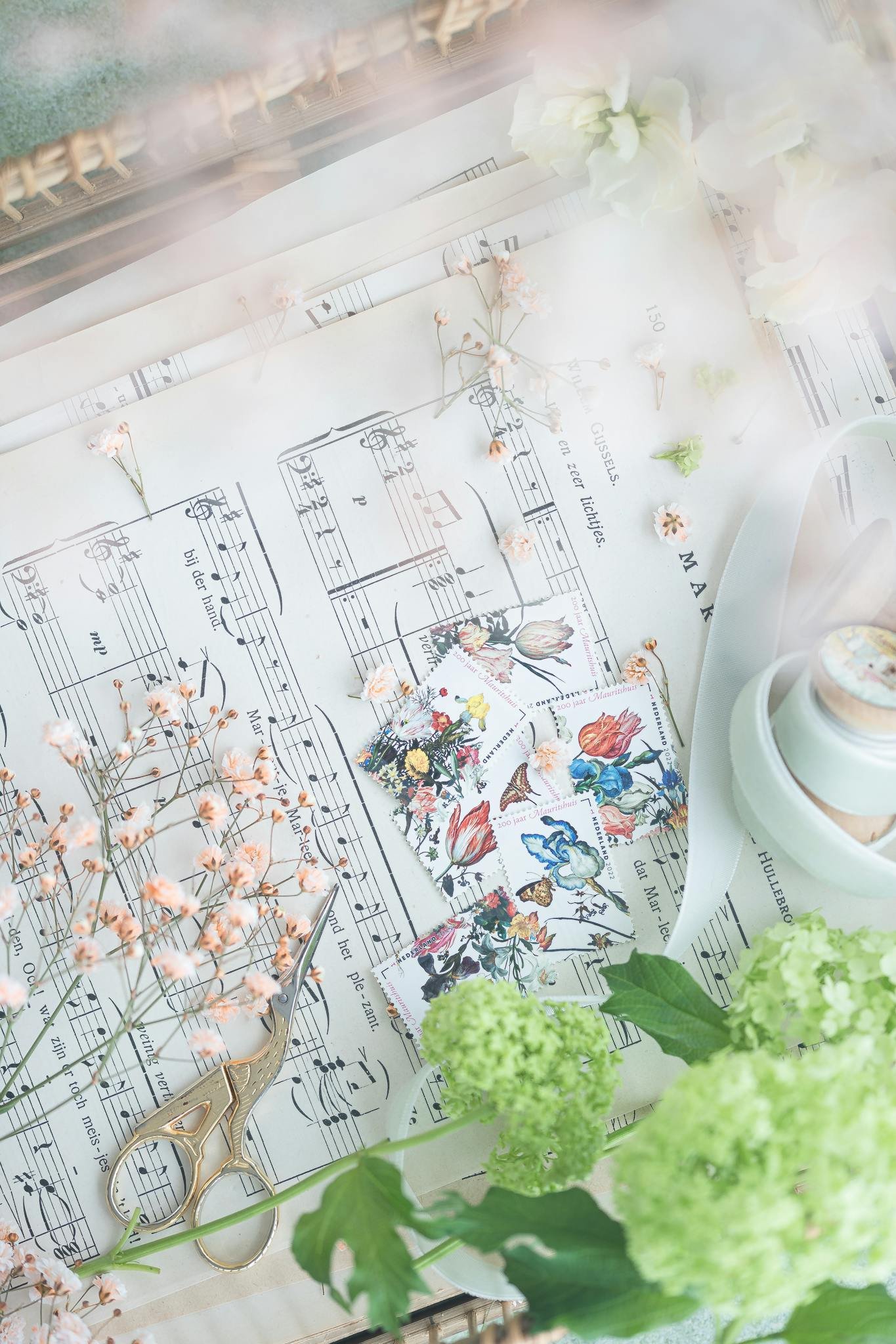 Delicate flatlay with flowers, music sheets, scissors, and decorative stamps.