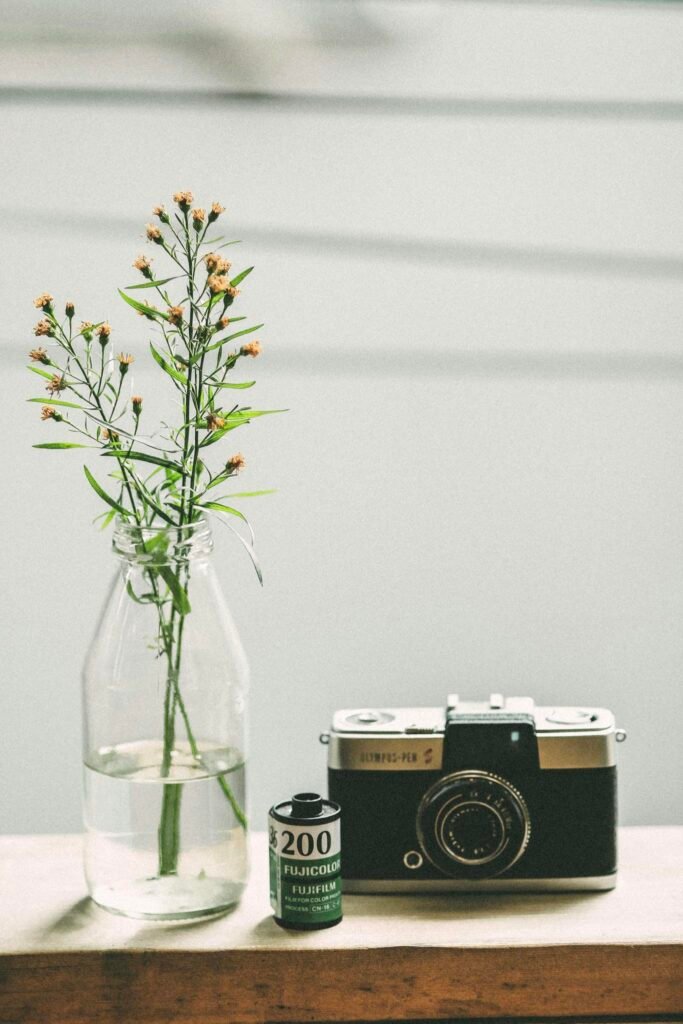 Elegant vintage camera and film roll beside a delicate floral arrangement in a glass vase.