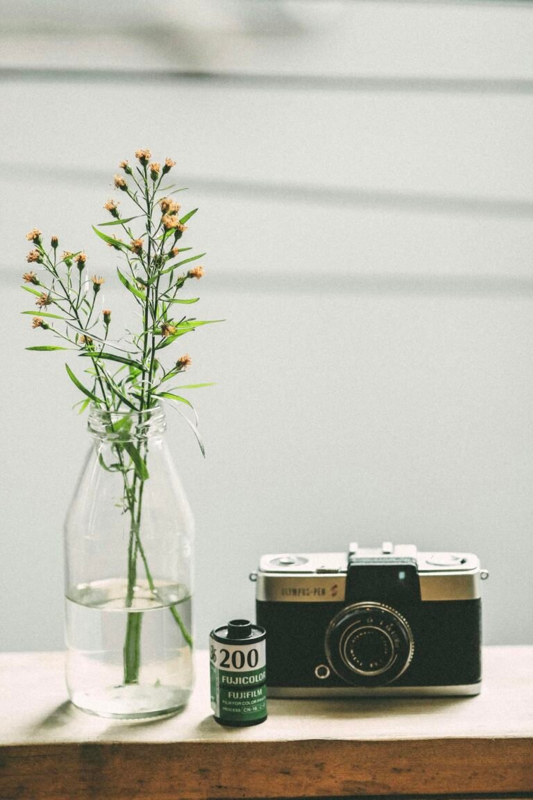 Elegant vintage camera and film roll beside a delicate floral arrangement in a glass vase.